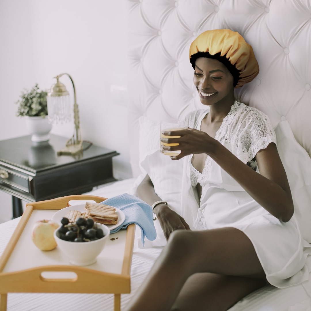 Woman wearing a yellow Lava Cap microwavable heat cap for deep conditioning dry hair while having breakfast in bed